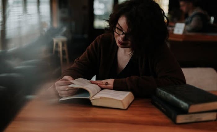 Woman reading a book about self-service knowledge base at a table, focused and immersed in reading.